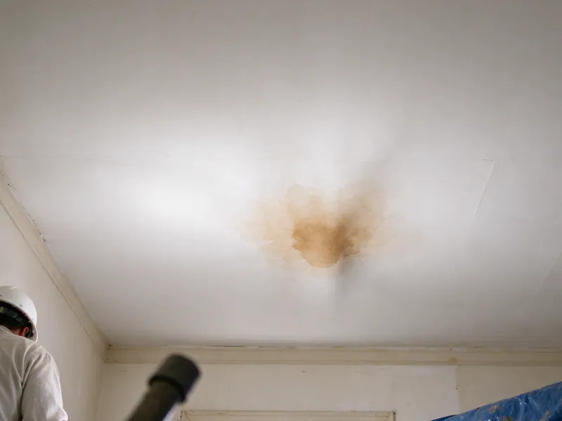 Brown water stain spreading on a white ceiling under a bathroom, in an older Columbus home